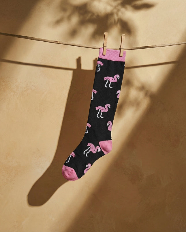 Black sock with pink flamingo pattern hanging on a clothesline against a beige wall.