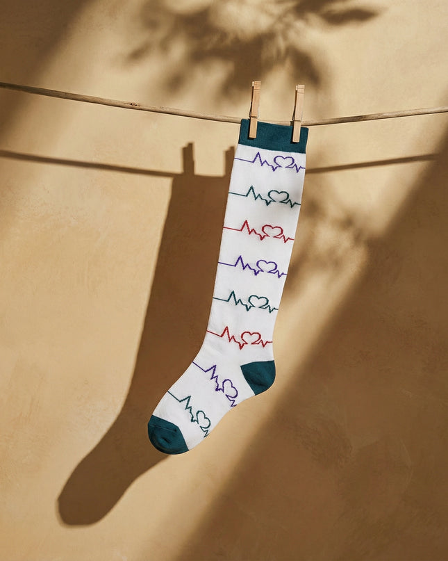 Knee-high sock with heart rate design hanging on a clothesline against a beige wall.