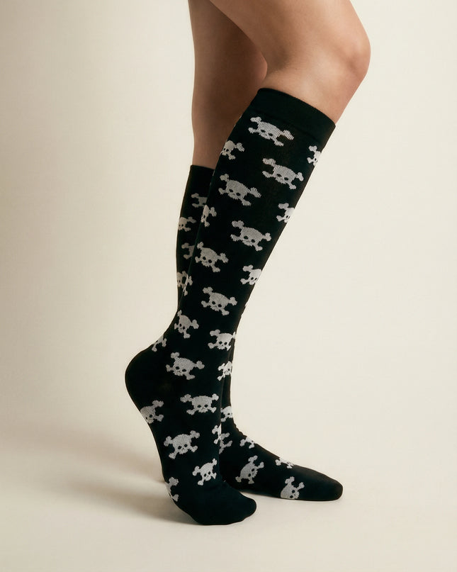 Black knee-high socks with white skull pattern worn by a person on a beige background