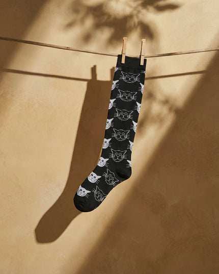 Black socks with white cat pattern hanging on a clothesline against a beige wall.
