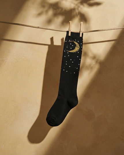 Black sock with gold moon and stars design hanging on a clothesline against a beige wall.