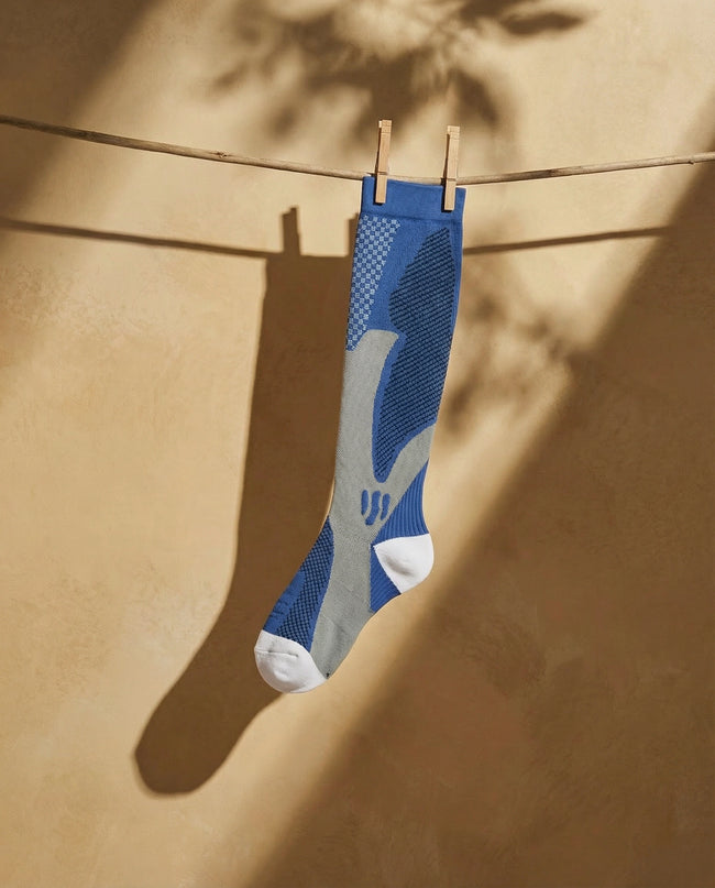 Blue and gray sock hanging on a clothesline against a beige wall.