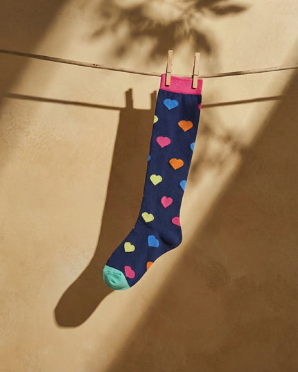 Navy sock with colorful hearts hanging on a clothesline against a beige wall.
