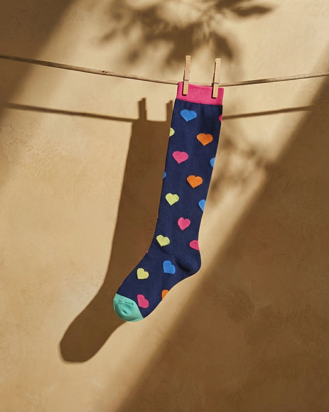 Navy sock with colorful hearts hanging on a clothesline against a beige wall.