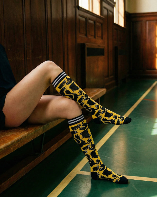Person wearing yellow knee-high socks with black patterns sitting on a wooden bench.