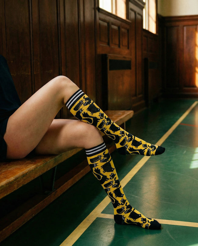 Person wearing yellow knee-high socks with black patterns sitting on a wooden bench.