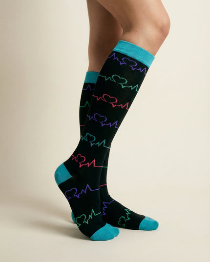 Black knee-high socks with colorful heart patterns and blue accents worn by a person on a beige background