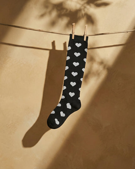 Black sock with white heart patterns hanging on a clothesline against a beige wall.