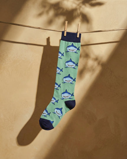 Green sock with shark pattern hanging on a clothesline against a beige wall.