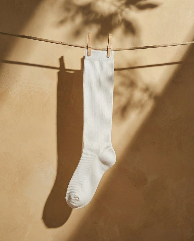 White sock hanging on a clothesline against a beige wall