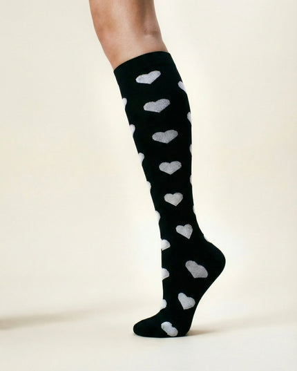 Black knee-high socks with white heart patterns worn by a person on a plain background