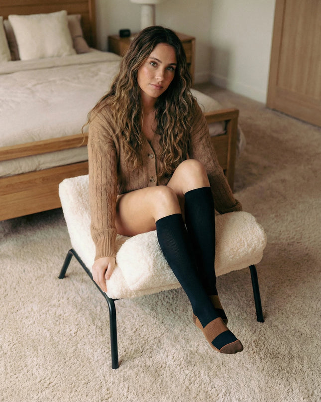 Woman sitting on a chair in a bedroom wearing knee-high socks.