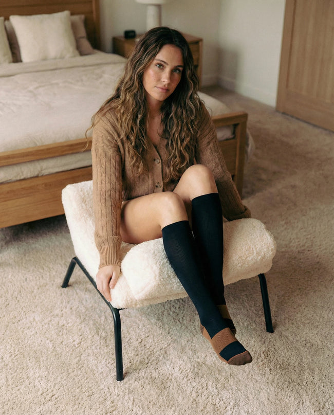 Woman sitting on a chair in a bedroom wearing knee-high socks.