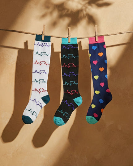 Three pairs of colorful socks hanging on a line against a beige wall.