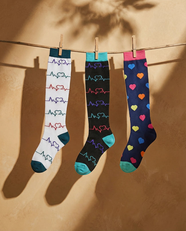 Three pairs of colorful socks hanging on a line against a beige wall.