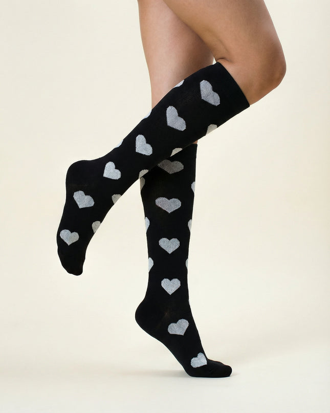 Black knee-high socks with heart patterns worn by a person on a beige background