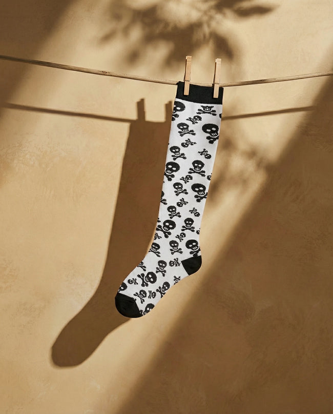 Skull-patterned sock hanging on a clothesline against a beige wall.