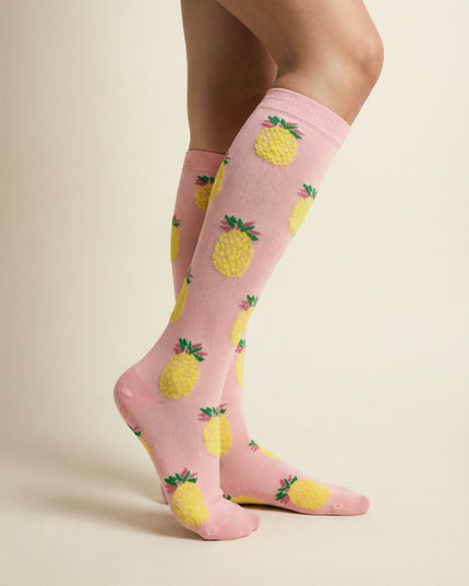 Pink socks with pineapple pattern worn by a person on a beige background