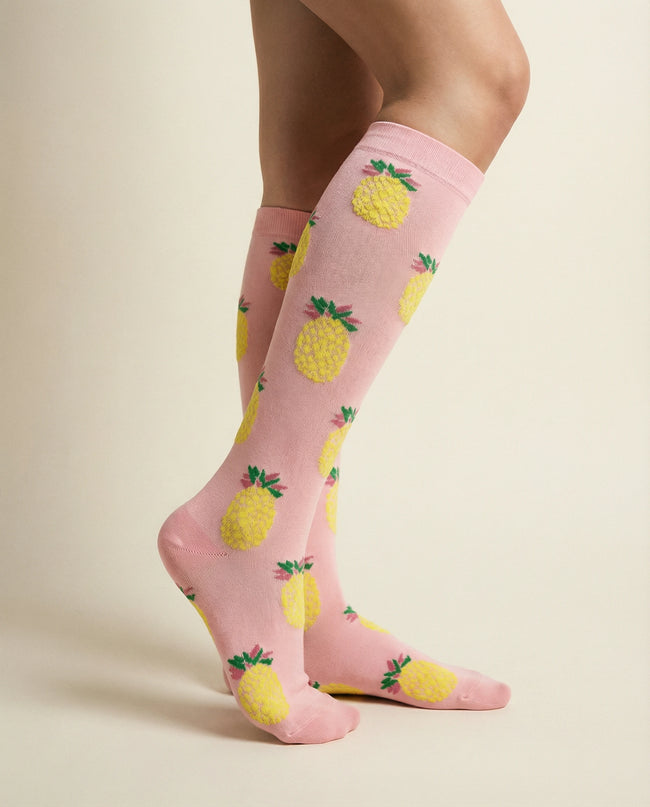 Pink socks with pineapple pattern worn by a person on a beige background