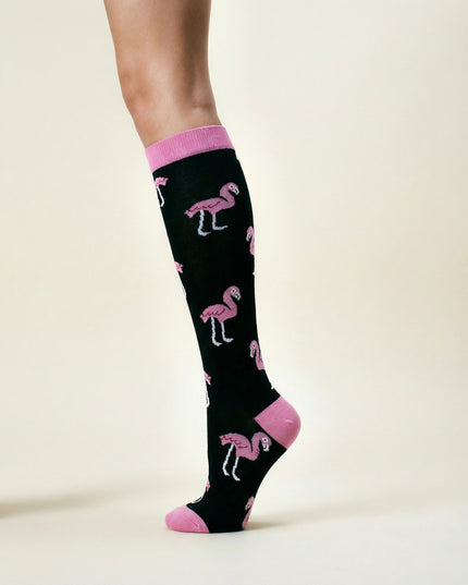 Black knee-high socks with pink flamingo pattern worn by a person on a beige background