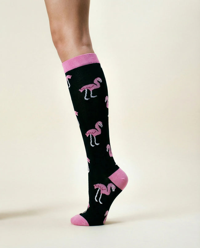 Black knee-high socks with pink flamingo pattern worn by a person on a beige background