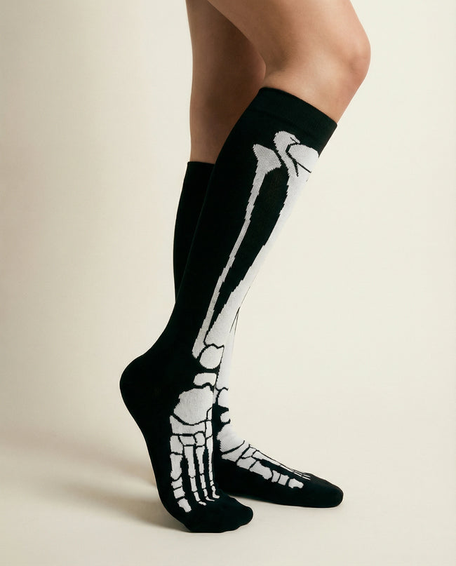Black socks with white skeleton design worn by a person on a beige background