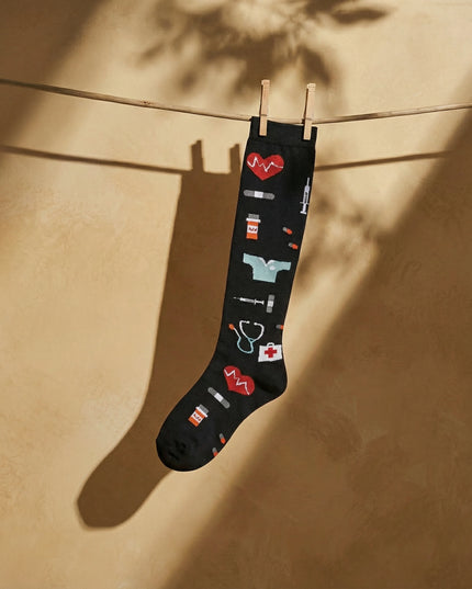 Black knee-high sock with medical-themed icons hanging on a clothesline against a beige wall.