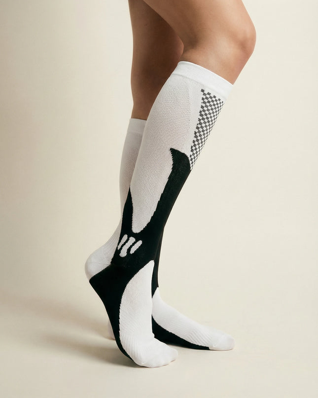 White knee-high socks with black and patterned design worn by a person on a beige background