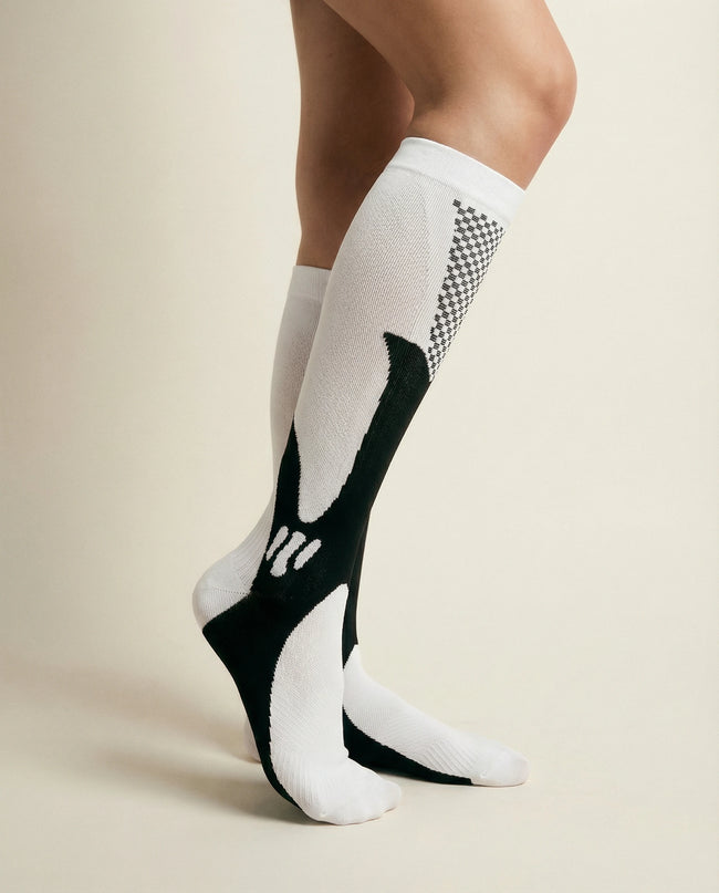 White knee-high socks with black and patterned design worn by a person on a beige background