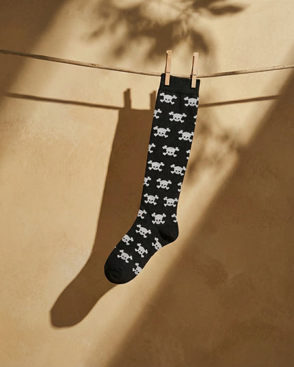 Black sock with white skull pattern hanging on a clothesline against a beige wall.