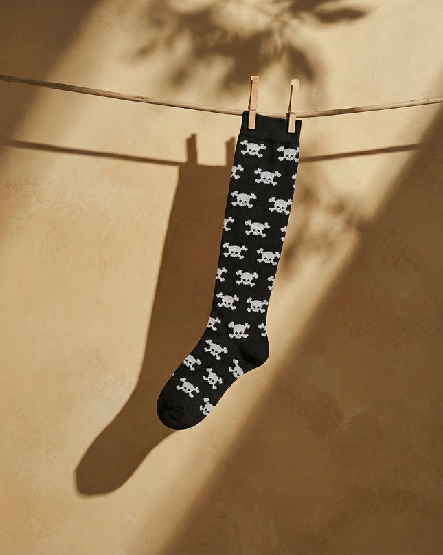 Black sock with white skull pattern hanging on a clothesline against a beige wall.