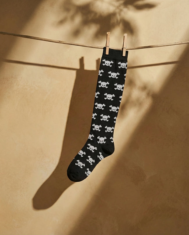 Black sock with white skull pattern hanging on a clothesline against a beige wall.