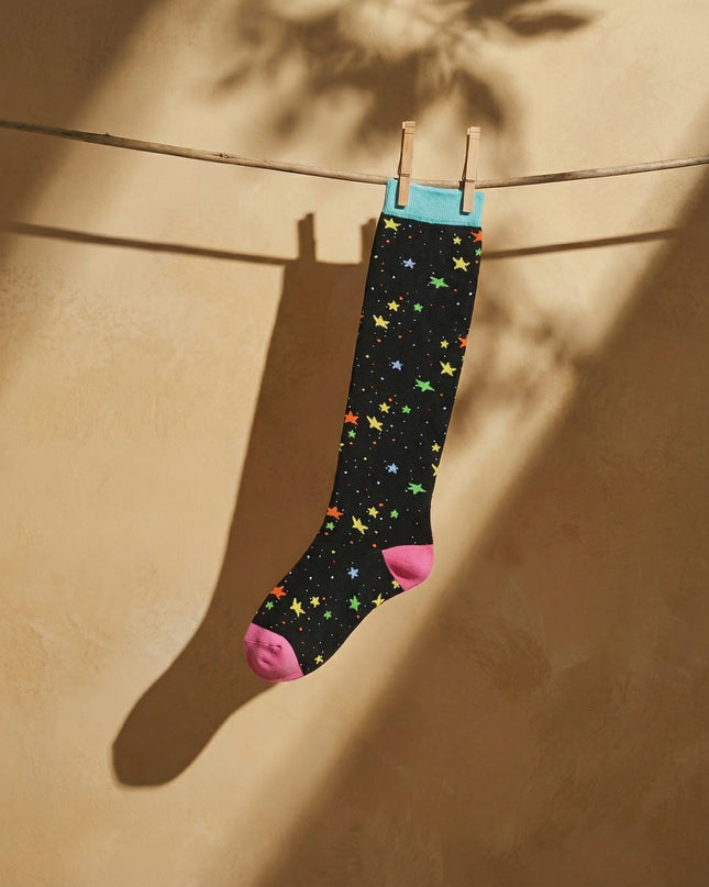 Colorful star-patterned sock hanging on a clothesline against a beige wall.