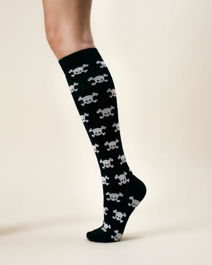 Black sock with white skull and crossbones pattern worn by a person on a beige background