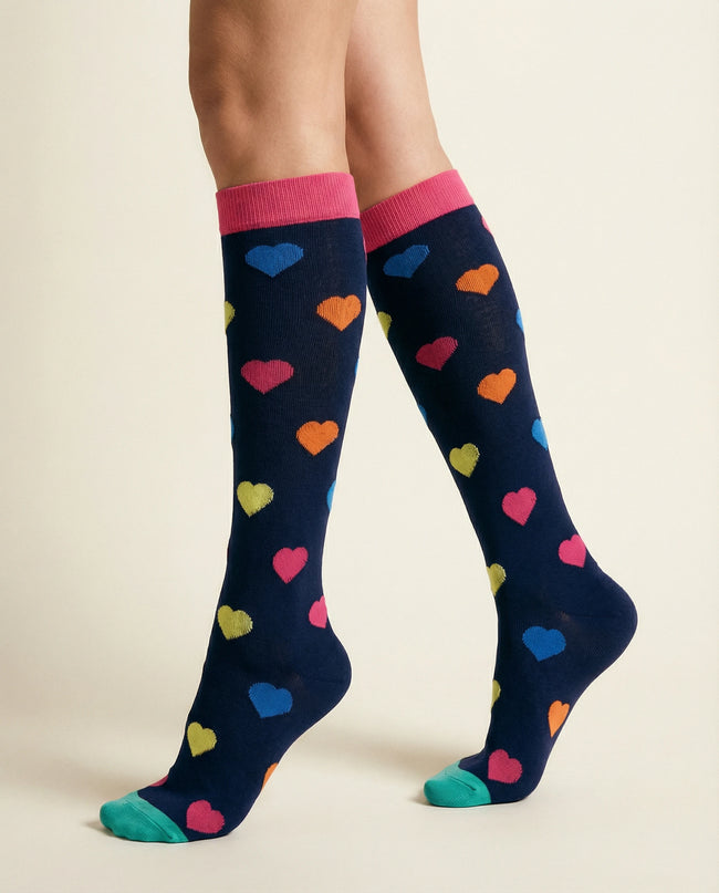 Navy knee-high socks with colorful heart pattern worn by a person on a beige background