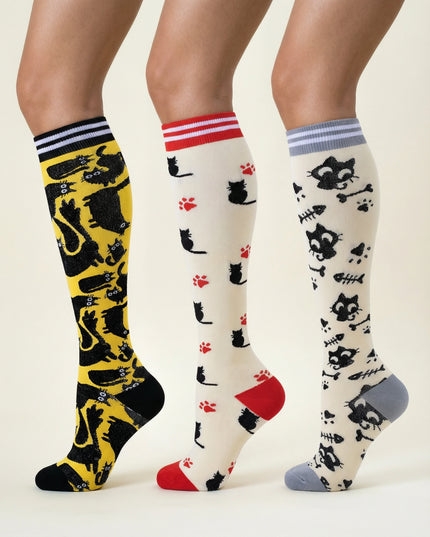 Three pairs of knee-high socks with cat patterns on a neutral background