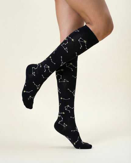 Black knee-high socks with white constellation patterns worn by a person on a beige background