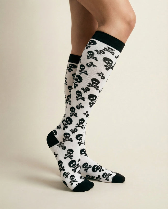 Knee-high socks with skull pattern worn by a person on a beige background