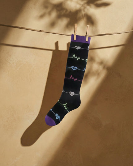 Black sock with colorful patterns hanging on a clothesline against a beige wall.