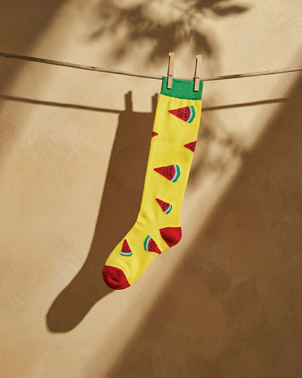 Yellow sock with watermelon pattern hanging on a clothesline against a beige wall.