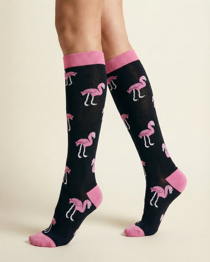 Black knee-high socks with pink flamingo pattern worn by a person on a beige background