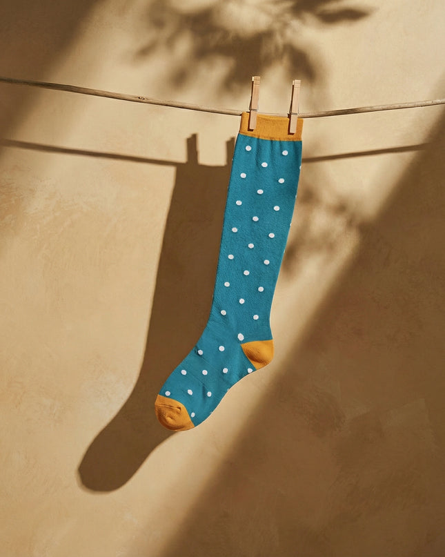 Blue sock with white polka dots hanging on a clothesline against a beige wall.