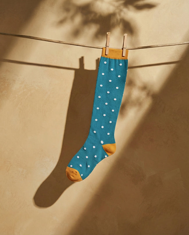 Blue sock with white polka dots hanging on a clothesline against a beige wall.