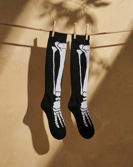 Black knee-high socks with white skeleton design hanging on a clothesline against a beige wall.