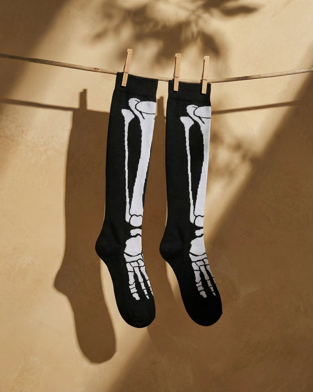 Black knee-high socks with white skeleton design hanging on a clothesline against a beige wall.
