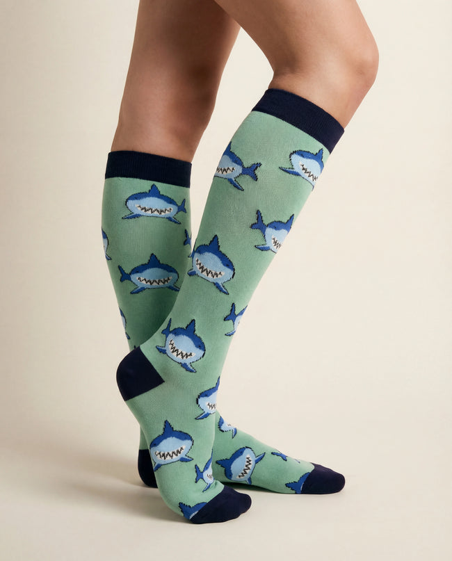 Green knee-high socks with shark pattern worn by a person on a beige background