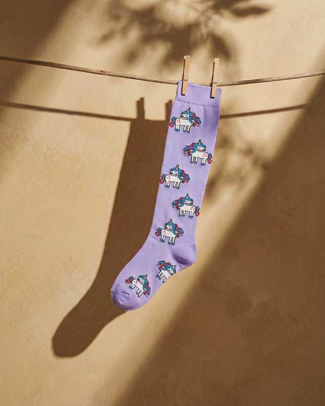 Purple sock with unicorn pattern hanging on a clothesline against a beige wall.