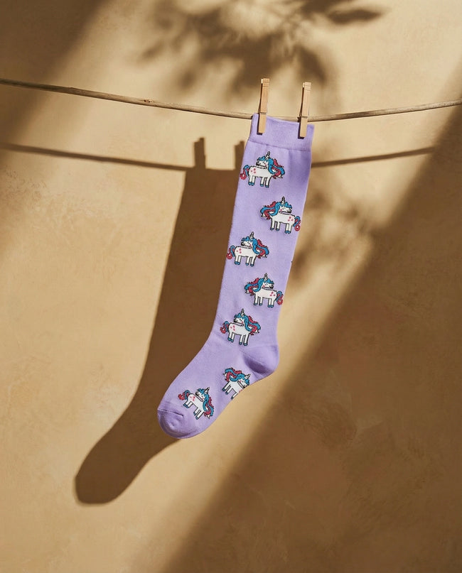 Purple sock with unicorn pattern hanging on a clothesline against a beige wall.
