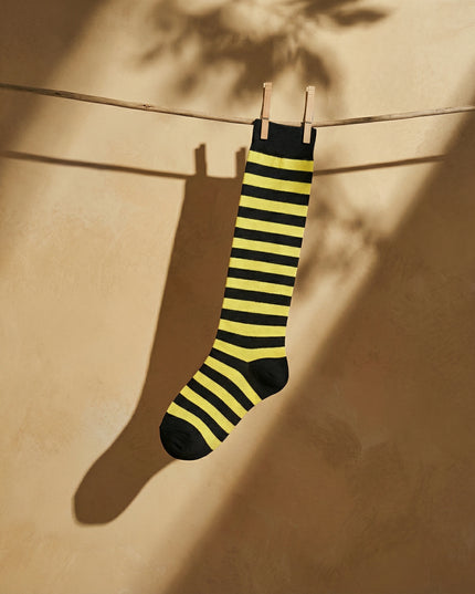 Yellow and black striped sock hanging on a clothesline against a beige wall.