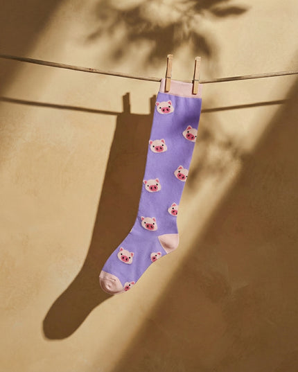 Purple sock with bear pattern hanging on a clothesline against a beige wall.